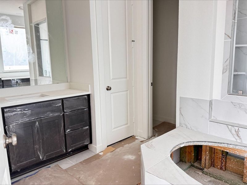 This inviting primary bath features a large vanity, classic cabinetry, and a relaxing soaking tub with elegant tile detailing.