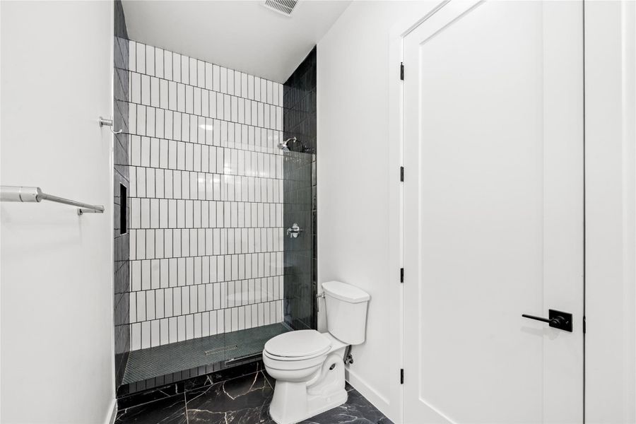Bathroom featuring a tile shower and dark marble finish floors