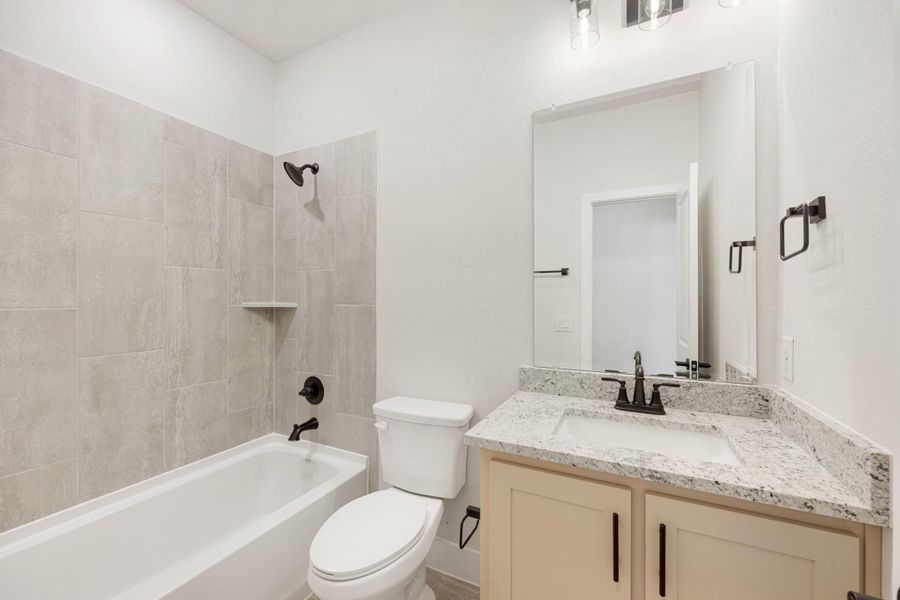 Bathroom with tiled tub and shower, granite vanity, white toilet, and matte black fixtures