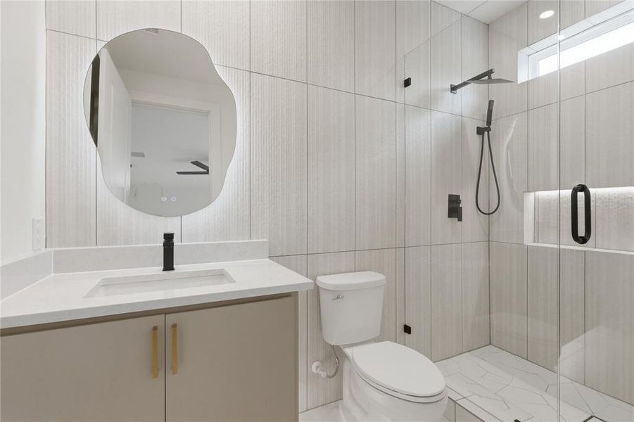 Bathroom featuring a contemporary floating vanity with an integrated sink and light-toned countertop, a frameless shower enclosure, and vertical plank-style wall tiling Bathroom featuring a contemporary floating vanity with an integrated sink and light-toned countertop, a frameless shower enclosure, and vertical plank-style wall tiling
