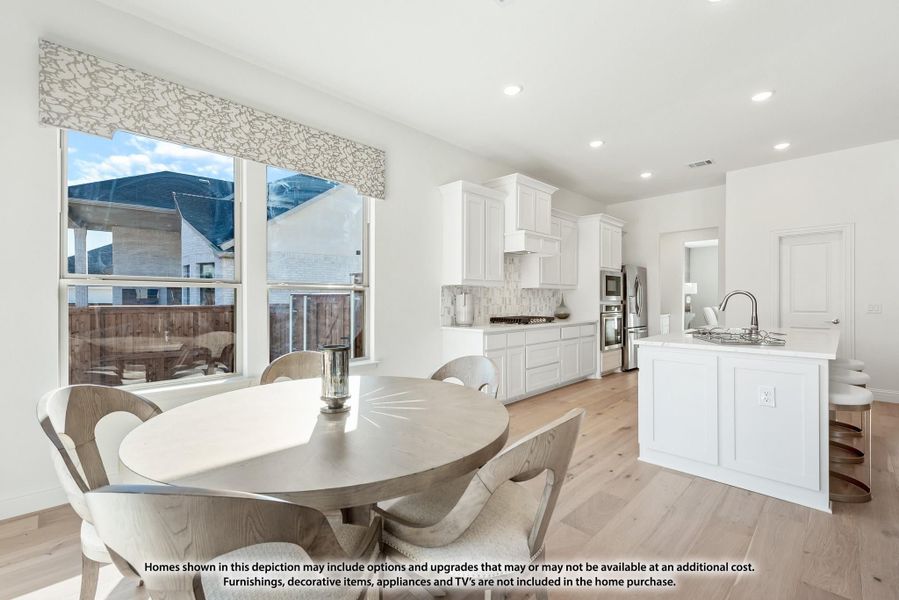 Open dining area with round table flows into kitchen with white cabinets, island, and light wood floors Open dining area with round table flows into kitchen with white cabinets, island, and light wood floors