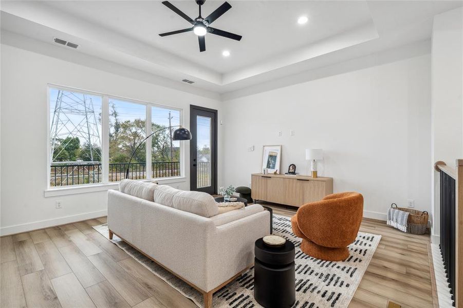 This living room offers an open and airy feel, with recessed tray ceilings and high ceilings that elevate the space, while large windows flood the room with natural light