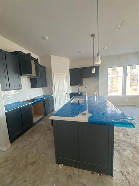 Kitchen with dark cabinets, an island with sink, hanging light fixtures, and decorative backsplash