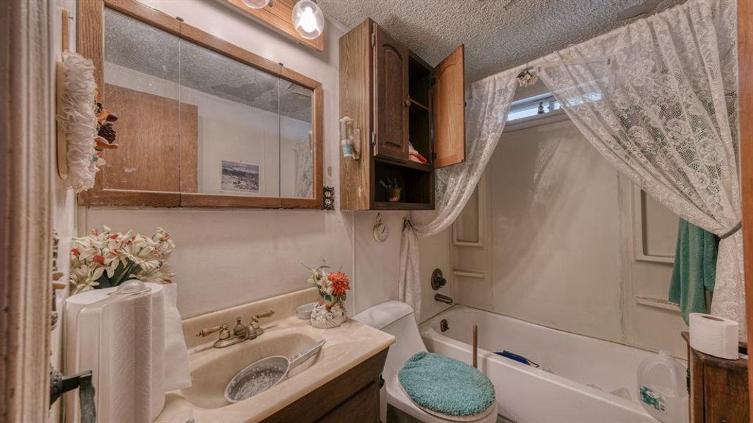 Full bathroom featuring toilet, vanity, a textured ceiling, and bathing tub / shower combination