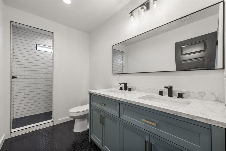 Full bath with double vanity, tiled shower, dark tile patterned floors, and recessed lighting