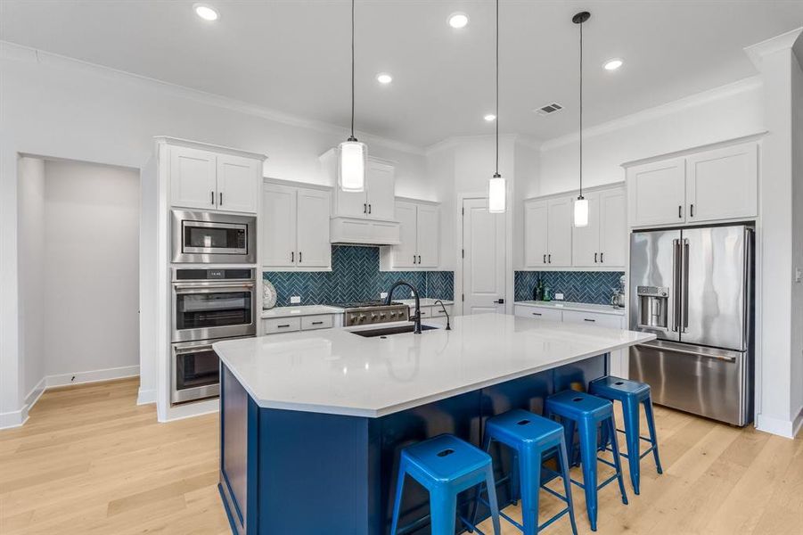 Kitchen featuring hanging light fixtures, a center island with sink, white cabinets, and stainless steel appliances