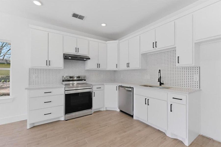 Kitchen with appliances with stainless steel finishes, white cabinetry, decorative backsplash, under cabinet range hood, and recessed lighting