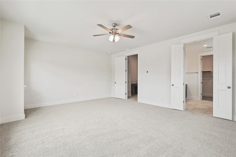 Unfurnished bedroom featuring a walk in closet, light colored carpet, and ceiling fan