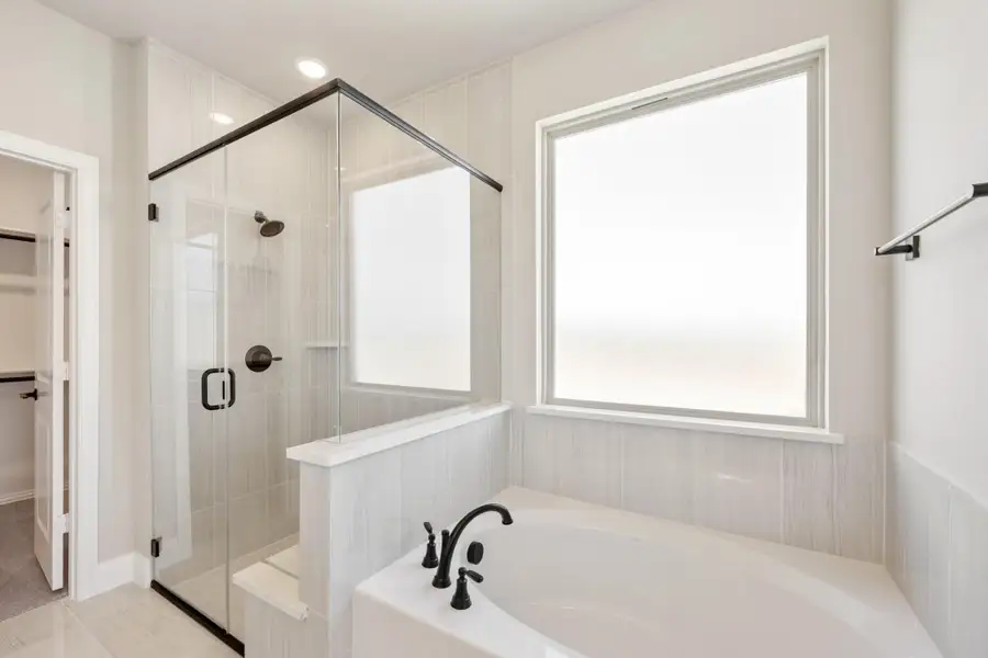 Master bathroom with soaking tub, glass-enclosed shower, tile walls, and black fixtures next to a walk-in closet Master bathroom with soaking tub, glass-enclosed shower, tile walls, and black fixtures next to a walk-in closet