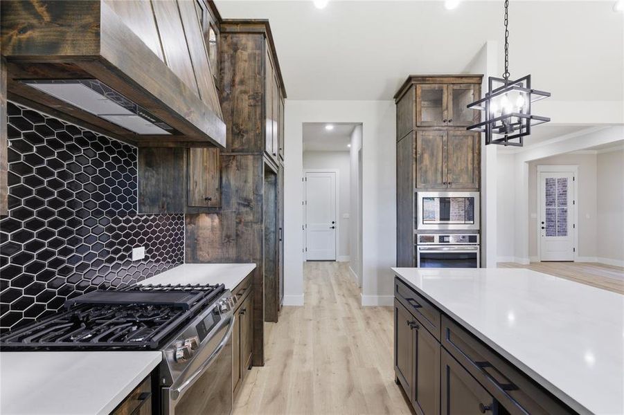 Gourmet kitchen featuring a gas range, custom wood cabinetry, hexagon tile backsplash, stainless steel appliances, and a large central island with a white countertop