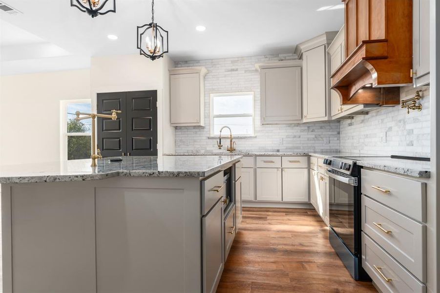 Kitchen featuring light stone counters, black electric range, light wood-style flooring, tasteful backsplash, and pendant lighting Kitchen featuring light stone counters, black electric range, light wood-style flooring, tasteful backsplash, and pendant lighting