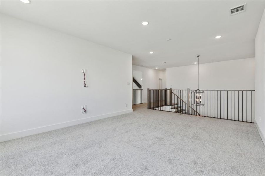 Spacious loft area featuring light gray carpeting, recessed lighting, and a modern black metal chandelier Spacious loft area featuring light gray carpeting, recessed lighting, and a modern black metal chandelier