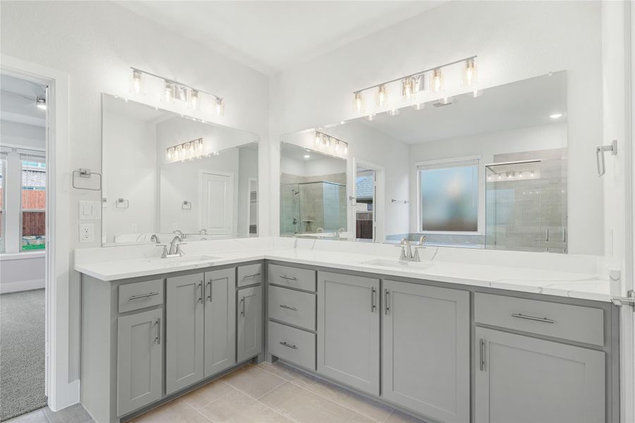 Master bathroom with dual sinks, gray L-shaped vanity, white countertops, and large mirrors with modern lighting fixtures.