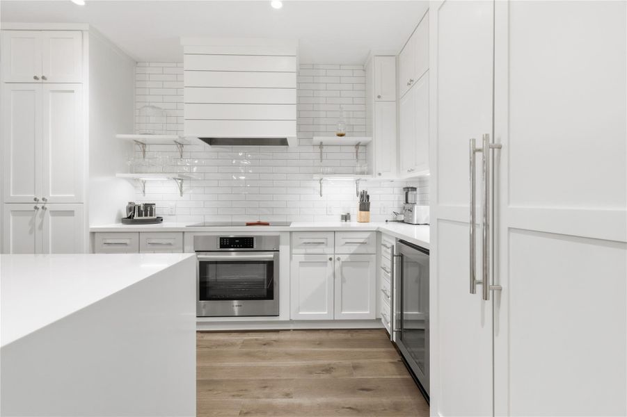 Kitchen with open shelves, oven, decorative backsplash, light stone countertops, and beverage cooler