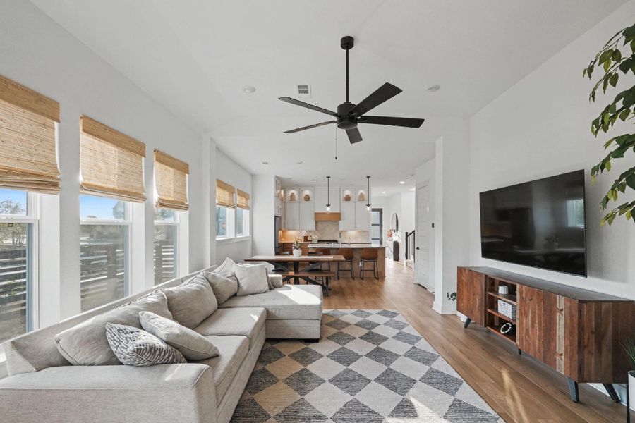 Spacious main living area with tall ceilings, wide-plank flooring, and a wall of windows that fills the home with natural light. The open sightlines connect to the dining and kitchen spaces, creating a bright and welcoming hub of the home.