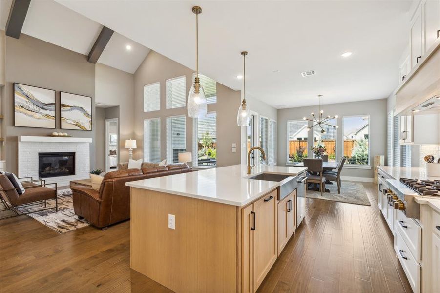 Kitchen featuring wood-type flooring, a kitchen island with sink, stainless steel gas cooktop, and a brick fireplace