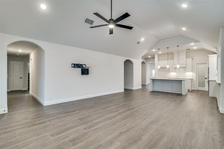 Spacious living room opens to the kitchen with light hardwood / wood-style floors, Plantation shutters, ceiling fan, and lofted ceiling