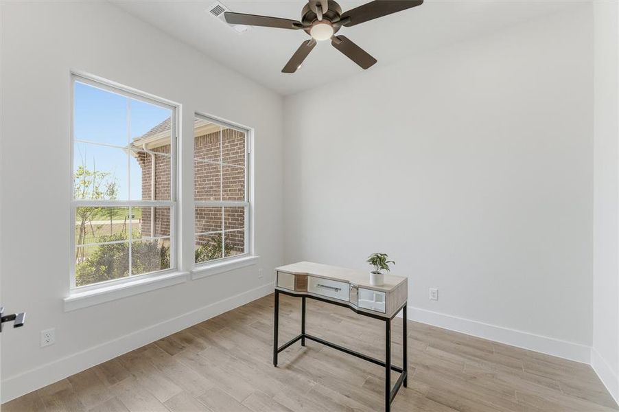 Bright interior space featuring two large windows, wood-finish flooring, crisp white walls, and a ceiling fan with integrated lighting