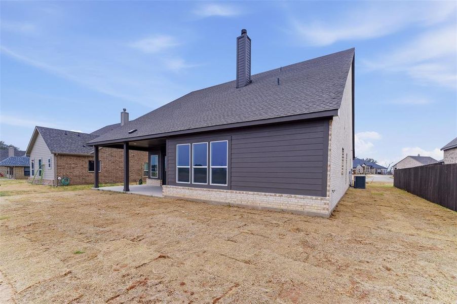 Rear view of house with a shingled roof, a patio, a chimney, and brick siding