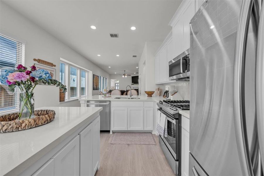 Modern kitchen featuring light wood-finish flooring, white cabinetry, and stainless steel appliances Modern kitchen featuring light wood-finish flooring, white cabinetry, and stainless steel appliances
