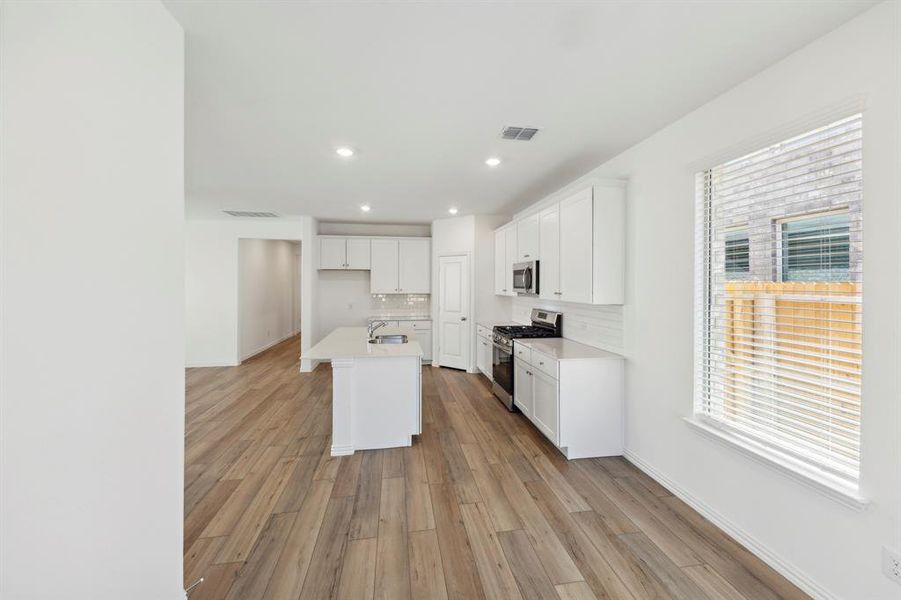 Kitchen featuring an island with sink, wood-type flooring, backsplash, and appliances with stainless steel finishes