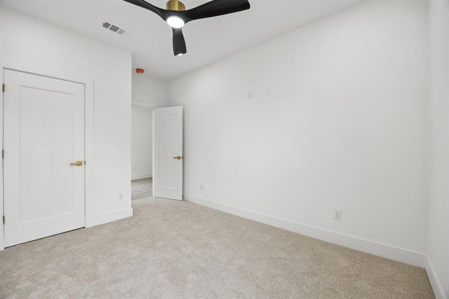 Neutral tone carpeting, white walls, and a modern ceiling fan with black blades and brass accents Neutral tone carpeting, white walls, and a modern ceiling fan with black blades and brass accents