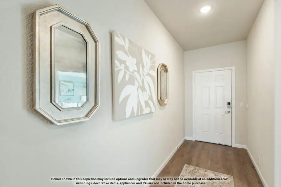 Narrow entryway hallway with hardwood floors, white front door, and decorative mirrors on beige walls