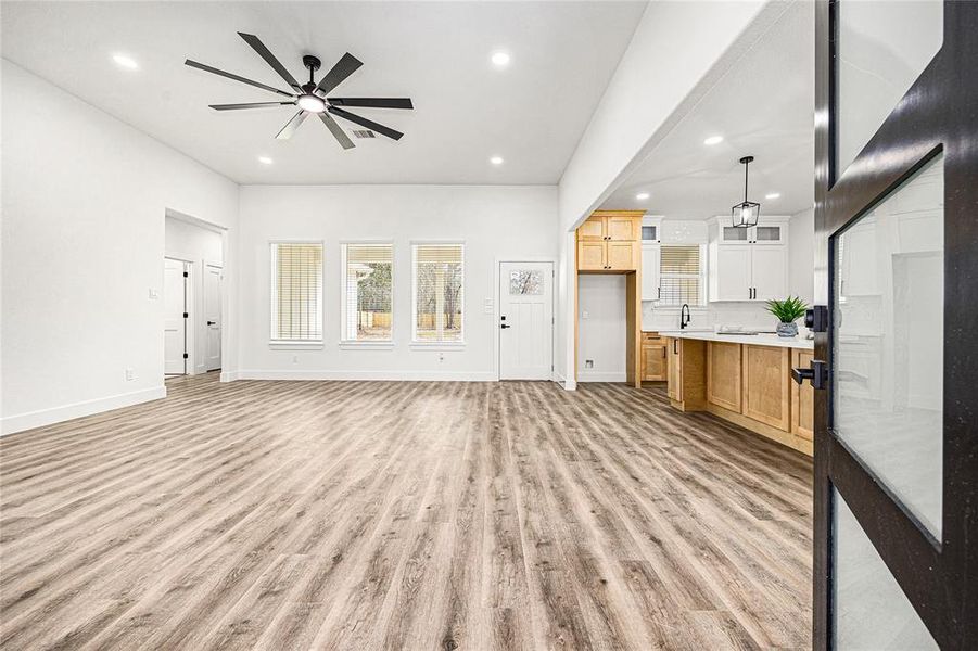 This photo showcases a spacious, open-concept living area with modern wood flooring, a large ceiling fan, and abundant natural light. The kitchen features stylish cabinetry, a breakfast bar, and pendant lighting, creating a welcoming atmosphere. The layout is ideal for entertaining and family living.