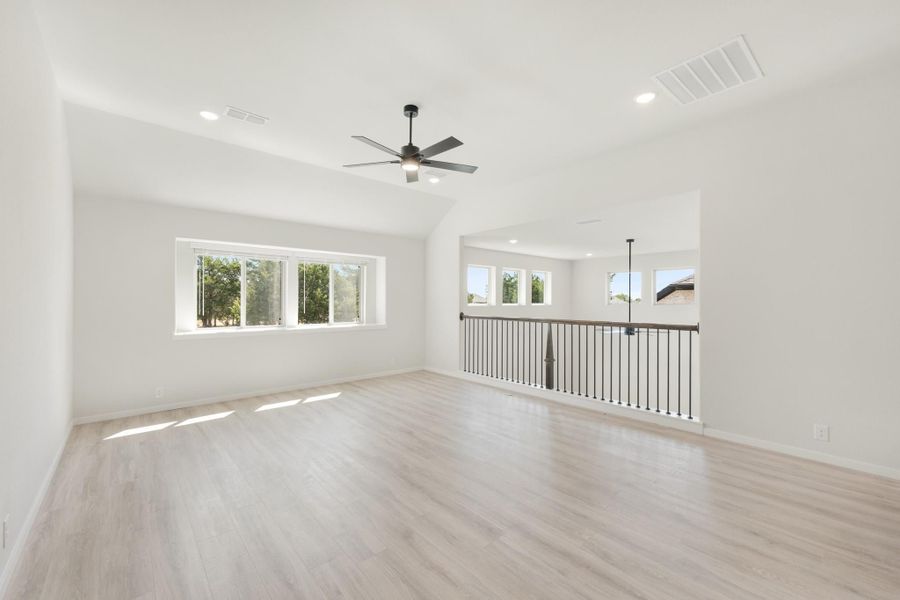Open upstairs loft with light wood floors, vaulted ceiling, ceiling fan, and metal stair railing