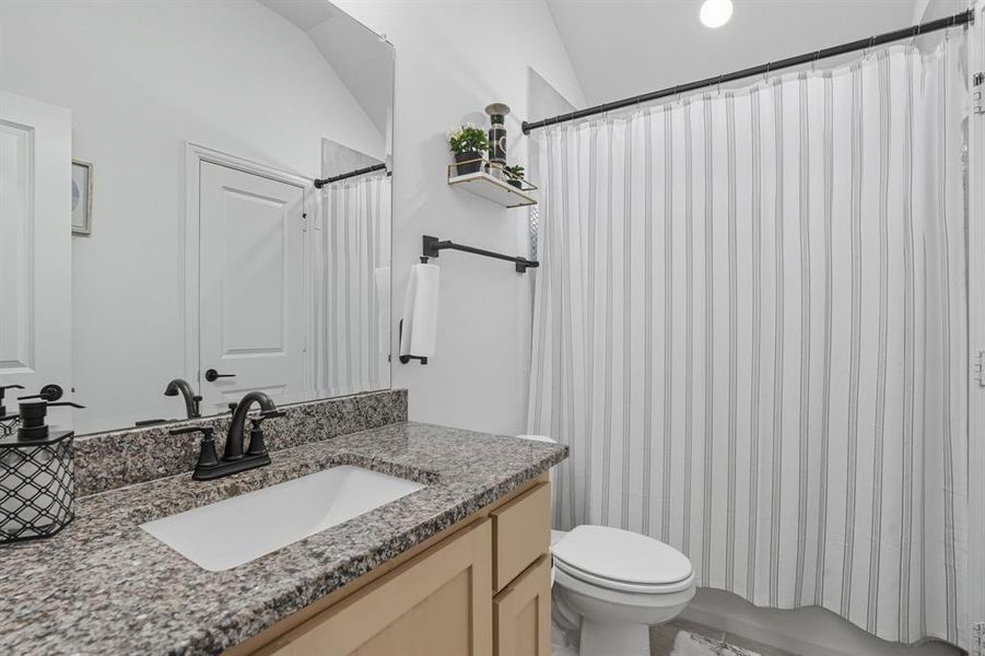 Bathroom featuring vanity, shower / tub combo, and vaulted ceiling