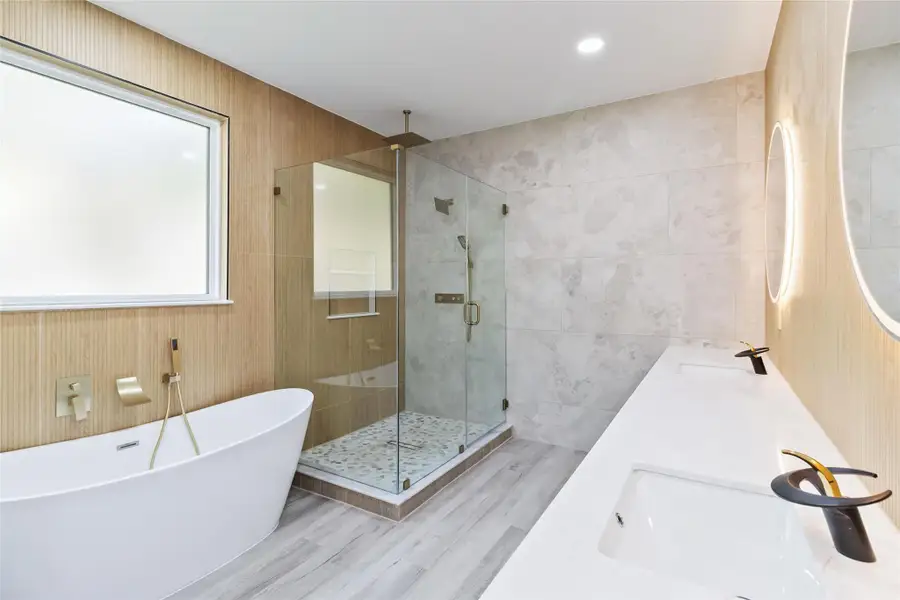 Bathroom with tile walls, a freestanding bath, a shower stall, double vanity, and recessed lighting