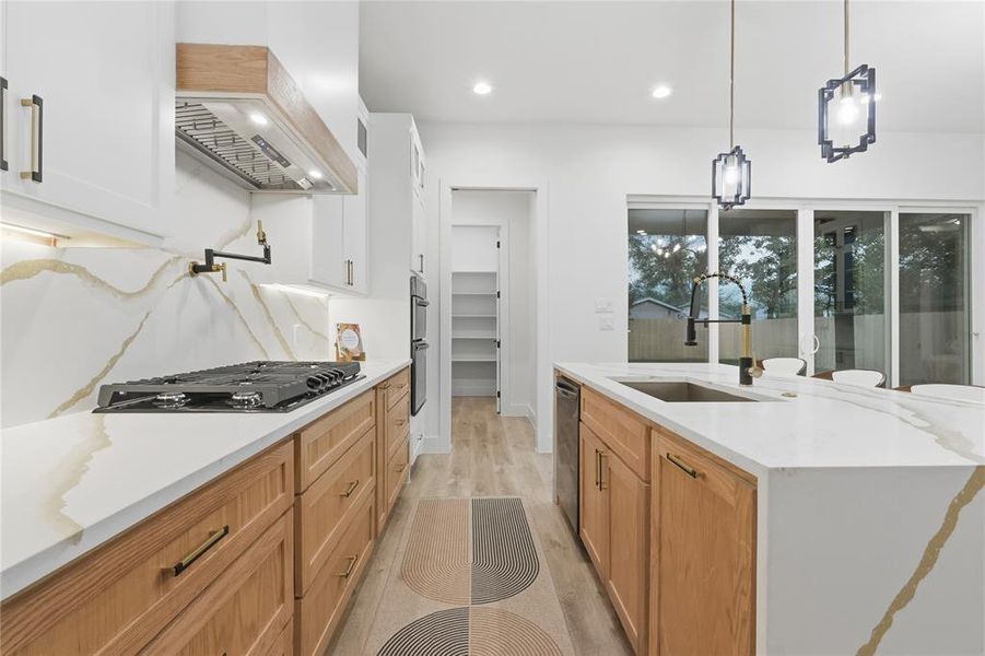 Kitchen with light stone countertops, light wood-type flooring, pendant lighting, an island with sink, and stainless steel appliances