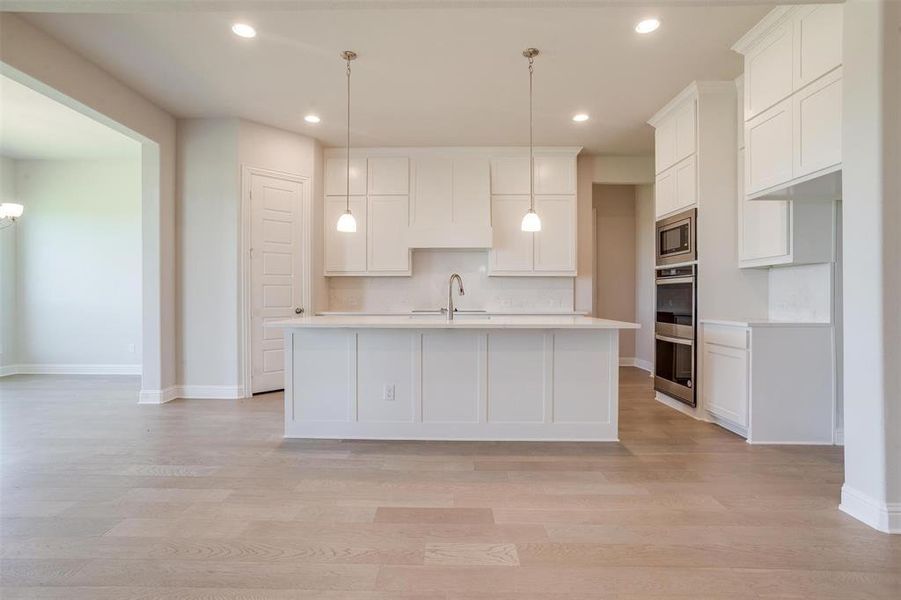 Kitchen featuring white cabinets, light wood-type flooring, decorative light fixtures, and appliances with stainless steel finishes