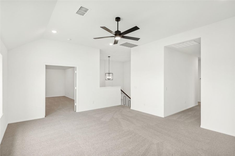 Spacious empty bedroom with vaulted ceiling, ceiling fan, carpet flooring, and open staircase landing nearby. Spacious empty bedroom with vaulted ceiling, ceiling fan, carpet flooring, and open staircase landing nearby.