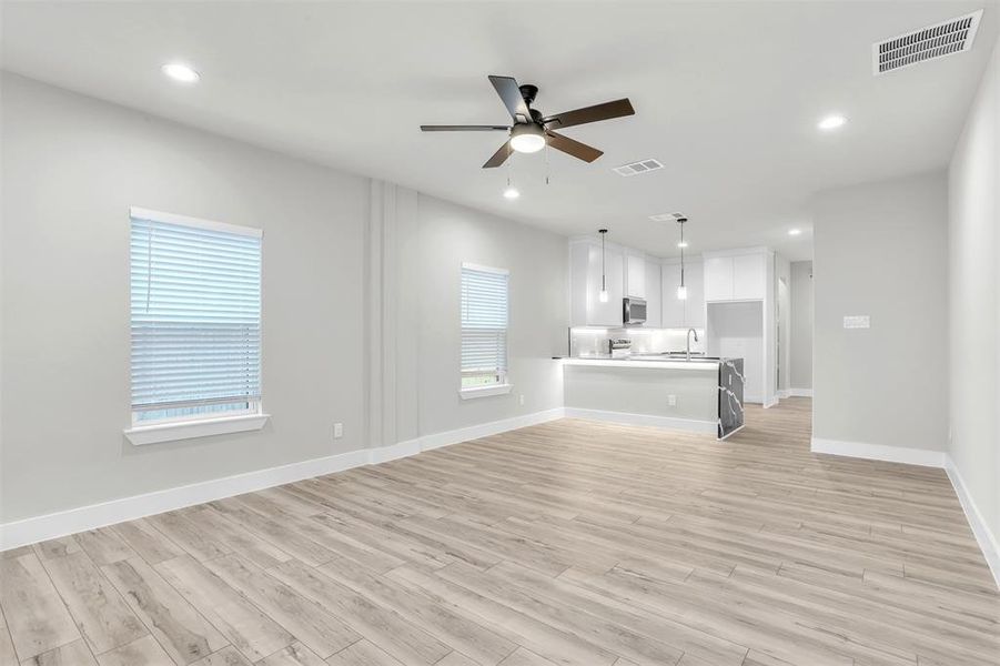 Unfurnished living room with plenty of natural light, ceiling fan, sink, and light wood-type flooring