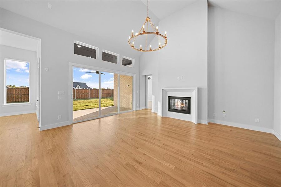 Unfurnished living room with high vaulted ceiling, a glass covered fireplace, light wood-style floors, and a chandelier Unfurnished living room with high vaulted ceiling, a glass covered fireplace, light wood-style floors, and a chandelier