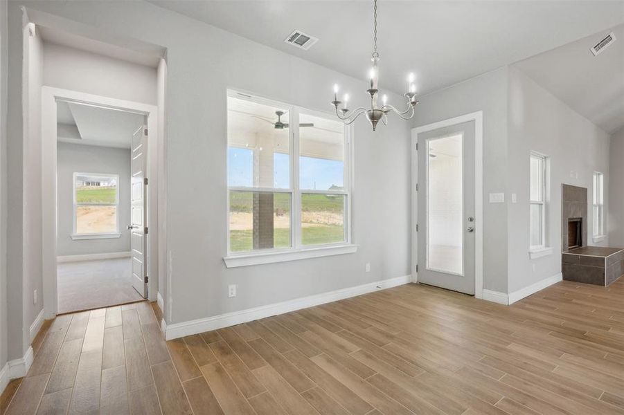 Unfurnished dining area featuring a notable chandelier, light hardwood / wood-style flooring, and a tiled fireplace