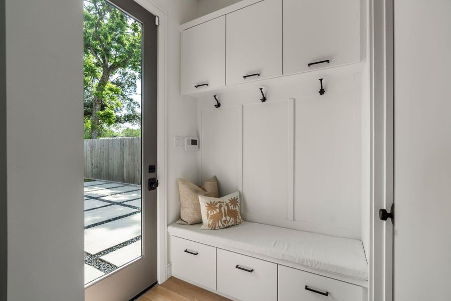 A convenient mud room is located just off the back door and features a built-in bench with a custom cushion, hook storage, upper cabinetry, lower drawers, and a walk-in storage closet.