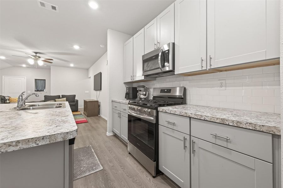 This modern kitchen features sleek granite countertops, stainless steel appliances, and white cabinetry. It opens into a cozy living area with a ceiling fan, creating a seamless flow for entertaining.