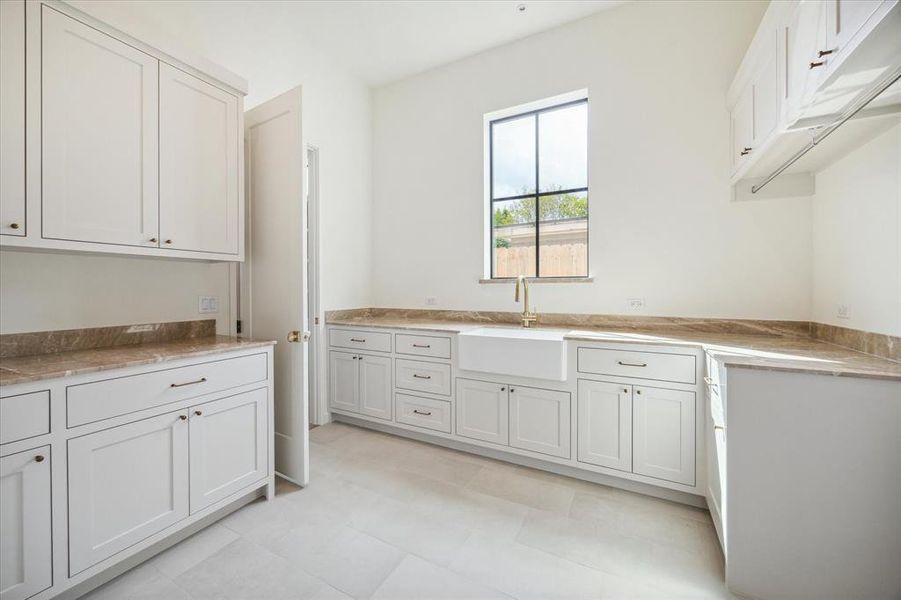 Generously sized laundry room with ample storage space, featuring custom cabinetry, Breccia Oniciata marble countertops, and a deep farmhouse sink. A large window provides great light and adds a welcoming touch to this functional space.