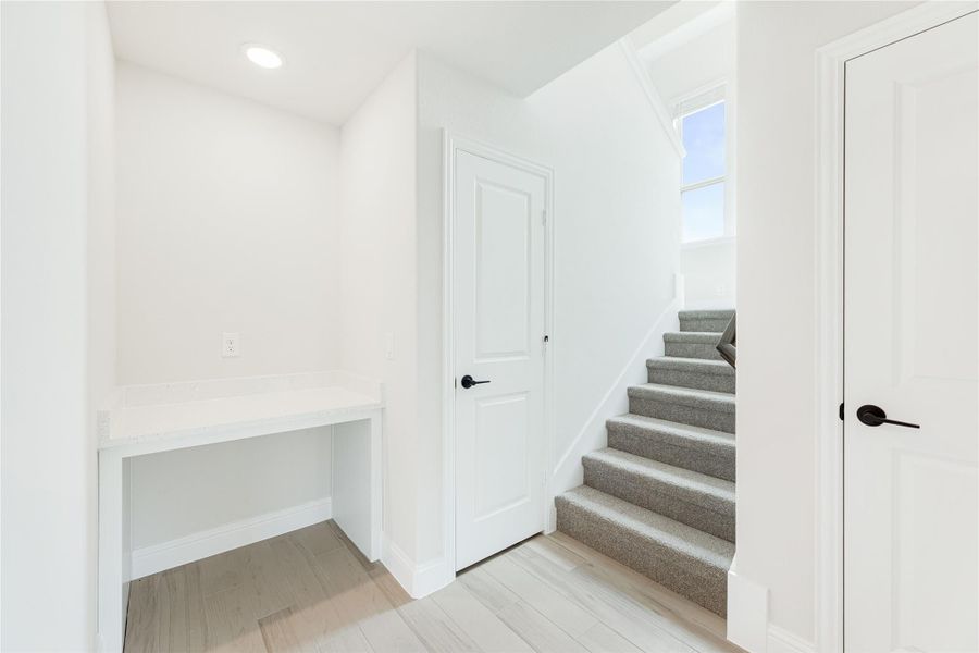 Hallway with built-in desk, carpeted staircase, and light hardwood floors in white-painted interior