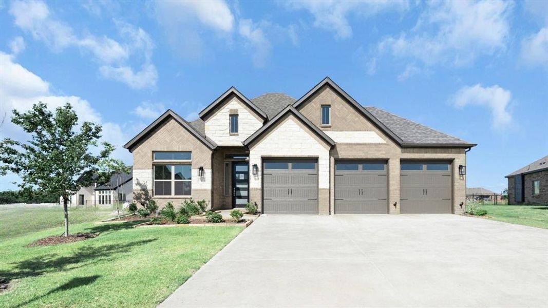 View of front of property featuring oversized driveway, brick and stone, and a 3-car garage.