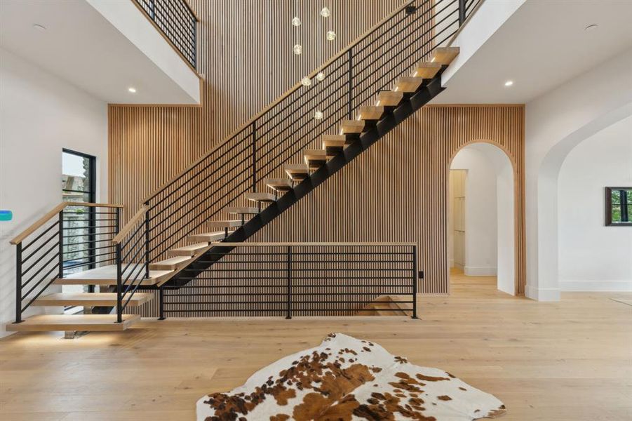 Staircase featuring a high ceiling, arched walkways, wooden accents walls, designer lighting, and white oak wood flooring Staircase featuring a high ceiling, arched walkways, wooden accents walls, designer lighting, and white oak wood flooring