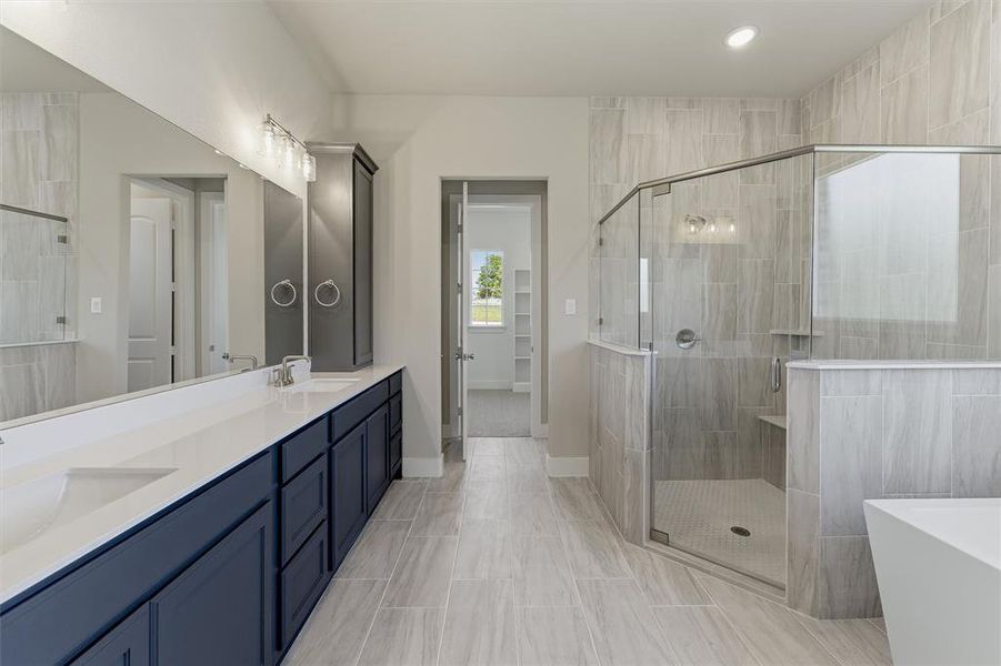 Bathroom featuring a dual vanity with dark cabinetry and white countertops, a frameless glass shower enclosure, and light wood-finish tile flooring
