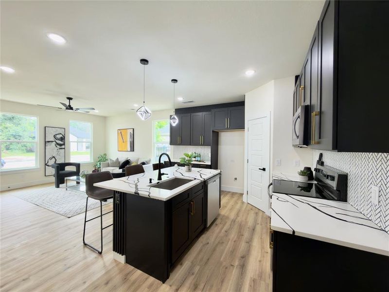Open-concept living space featuring a modern kitchen with black cabinetry, white countertops with black veining, a herringbone tile backsplash, and light wood-finish flooring