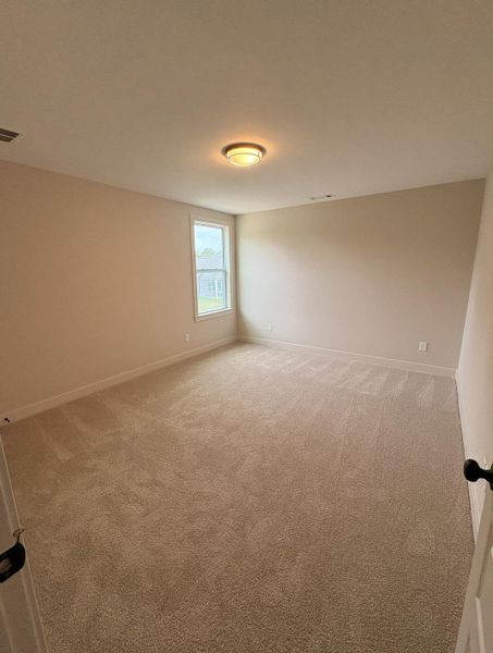 Spacious room featuring neutral carpeting, light-toned wall paint, a single window with white trim, and a flush-mount ceiling light fixture