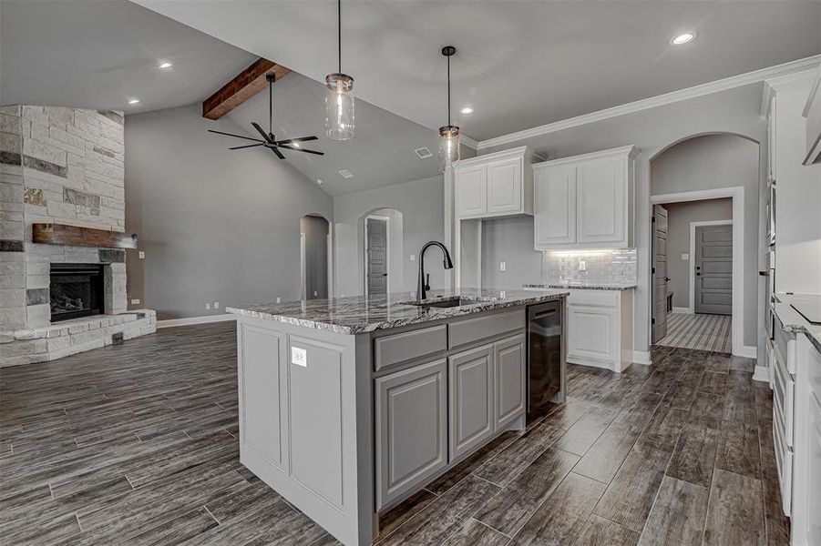 Kitchen featuring white cabinetry, wine cooler, an island with sink, sink, and backsplash