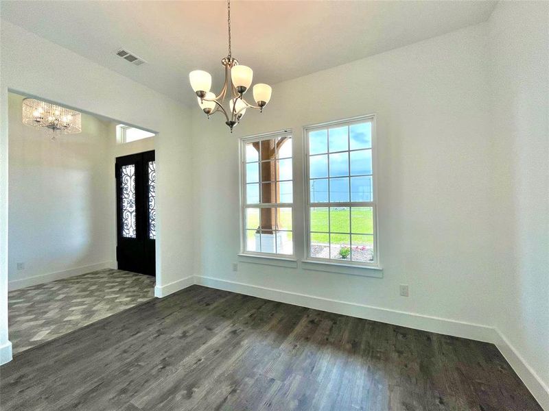 Unfurnished dining area featuring dark wood-type flooring, visible vents, a notable chandelier, and a healthy amount of sunlight Unfurnished dining area featuring dark wood-type flooring, visible vents, a notable chandelier, and a healthy amount of sunlight