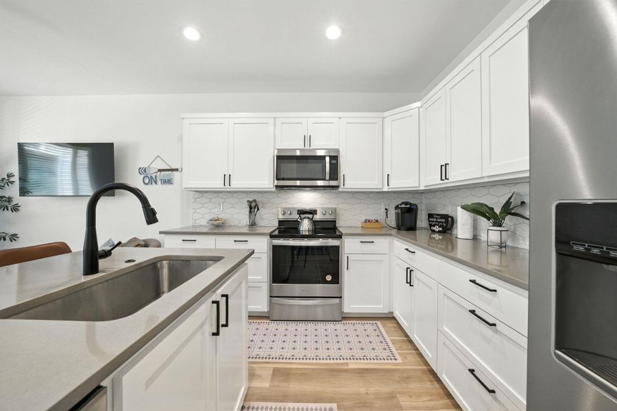 Kitchen with stainless steel appliances, tasteful backsplash, white self-close cabinets, light vinyl plank flooring and recessed lighting Kitchen with stainless steel appliances, tasteful backsplash, white self-close cabinets, light vinyl plank flooring and recessed lighting