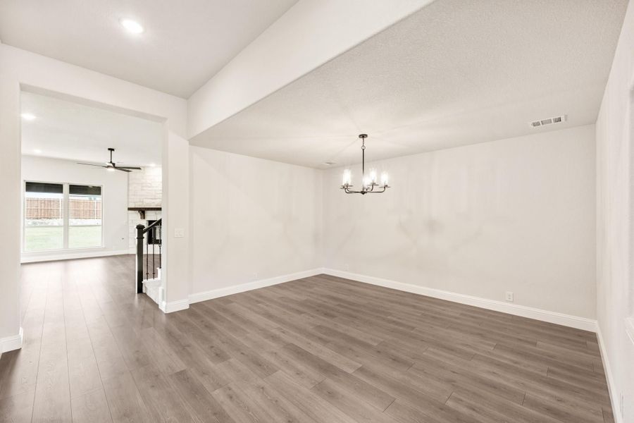Empty dining room with chandelier, hardwood floors, and open view to living area with ceiling fan